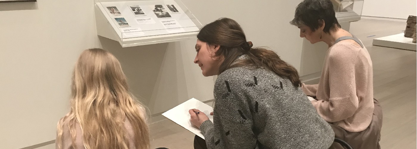 Three individuals seated on stools and sketching in the Wallach Art Gallery