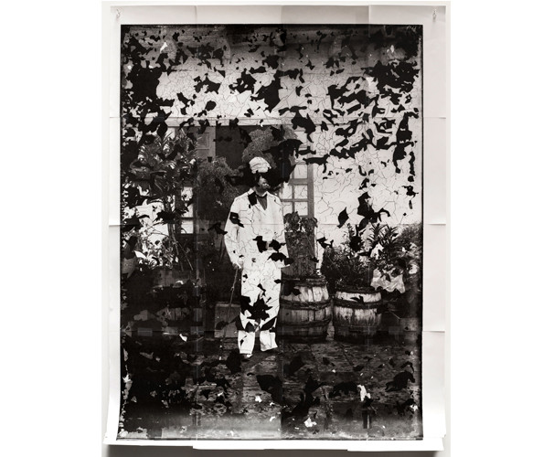 Stephanie Syjuco, "Fragment: Military Officer (from Alexander Schadenberg photographs of the Philippines, circa 1881-1896, National Anthropology Archives, NAA.PhotoLot.15)," 2021. Archival pigment inkjet print; 52 1/2 x 40 1/2 in. Courtesy of the artist; RYAN LEE Gallery, NY; and Catharine Clark Gallery, San Francisco. An artwork by the artist Stephanie Syjuco, an archival photograph of a military officer is overlaid with black shapes recalling the shapes made by the crackling plaster on the building he stands in front of.