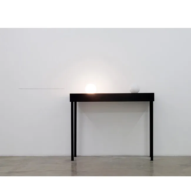 Iman Issa. Material for a sculpture proposed as an alternative to a monument that has become an embarrassment to its people, 2010. Two lightbulbs, plywood table, and vinyl text on the wall; 59 x 47-1/2 x 19-3/4 inches. Courtesy the artist and Rodeo Gallery.